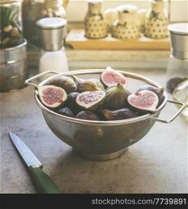 Fig halves in sieve on grey kitchen table with knife and kitchen utensils in background. Preparing healthy Mediterranean fruit at home. Front view.