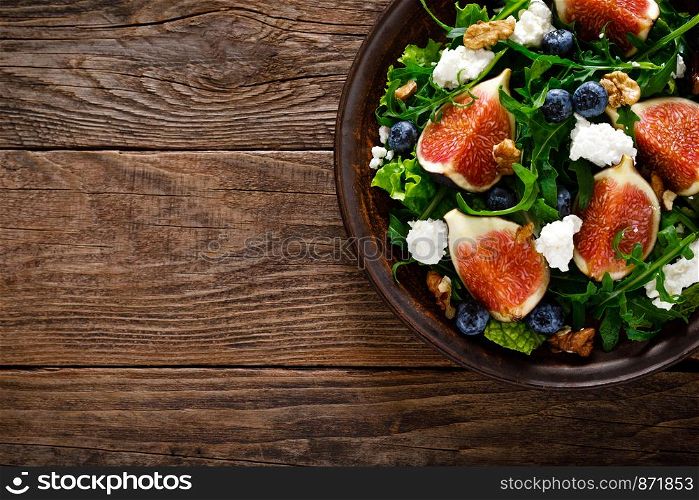 Fig salad with goat cheese, blueberry, walnuts and arugula on wooden background. Healthy food. Top view