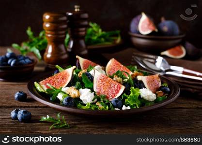 Fig salad with goat cheese, blueberry, walnuts and arugula on wooden background. Healthy food. Lunch