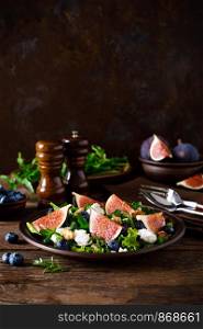 Fig salad with goat cheese, blueberry, walnuts and arugula on wooden background. Healthy food. Lunch