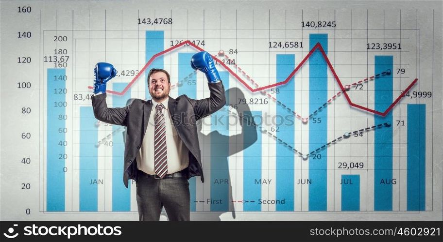Fighting for sales figures. Young businessman in boxing gloves and infographs at background