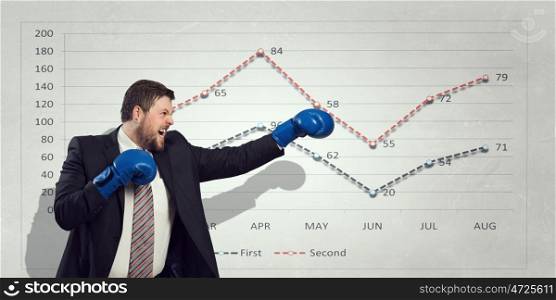 Fighting for sales figures. Young businessman in boxing gloves and infographs at background