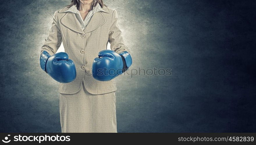 Fighting for success. Young confident businesswoman wearing blue boxing gloves