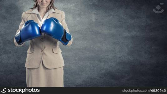 Fighting for success. Young confident businesswoman wearing blue boxing gloves