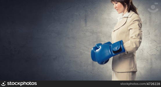 Fighting for success. Young confident businesswoman wearing blue boxing gloves