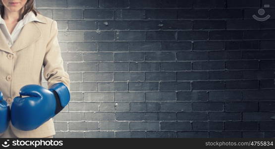 Fighting for success. Young confident businesswoman wearing blue boxing gloves