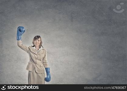 Fighting for success. Young confident businesswoman wearing blue boxing gloves