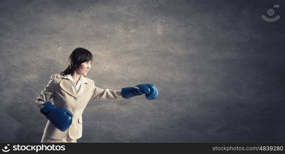 Fighting for success. Young confident businesswoman wearing blue boxing gloves