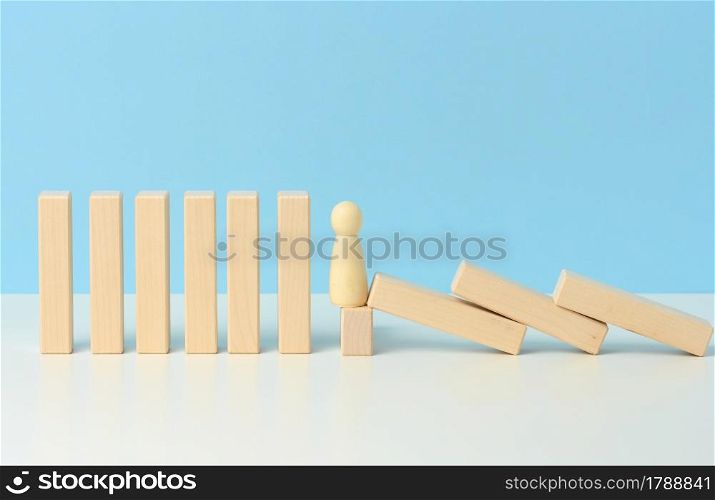 figures of men restrain the falling of wooden blocks, the effect of dominoes on a blue background. concept of teamwork, ability to prevent the consequences of the influence of external sources