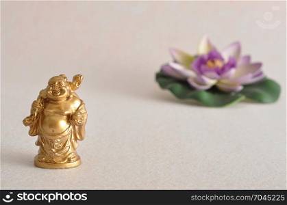 Figurine of a laughing and cheerful golden Buddha with an out of focus Lotus flower