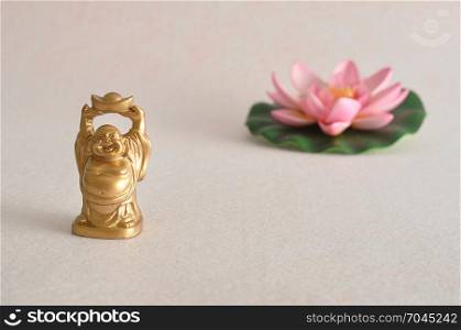 Figurine of a laughing and cheerful golden Buddha with an out of focus Lotus flower