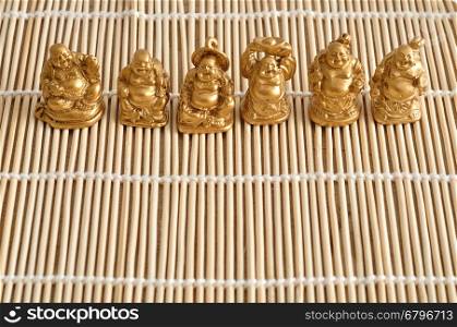 Figurines of laughing and cheerful golden Buddhas isolated on a bamboo background
