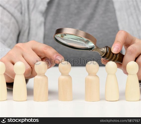 figurines of men on a white table, a female hand holds a magnifying glass over one. concept of searching for employees in the company, recruiting personnel, identifying talented and strong personalities