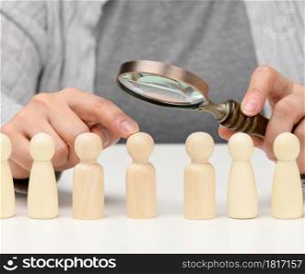 figurines of men on a white table, a female hand holds a magnifying glass over one. concept of searching for employees in the company, recruiting personnel, identifying talented and strong personalities