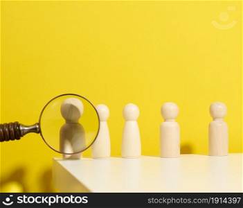 figurines of men on a white table and magnifying glass. Concept of searching for employees in the company, recruiting personnel, identifying talented and strong personaliti