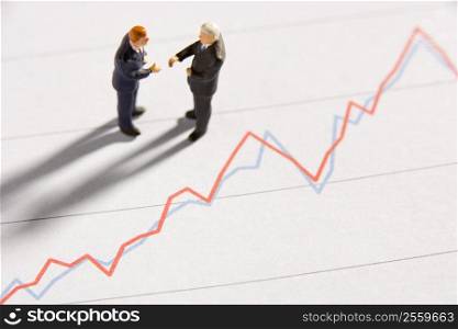 Figurines Of Two Businessmen Shaking Hands On A Line Graph