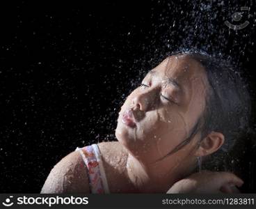 file of face of asian girl playing with pouring water with black background. face of asian girl playing with pouring water with black background