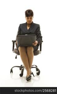 Filipino middle-aged businesswoman sitting in office chair with laptop against white background.