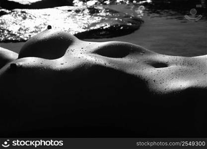 Filipino young nude woman lying in water on rocky beach.