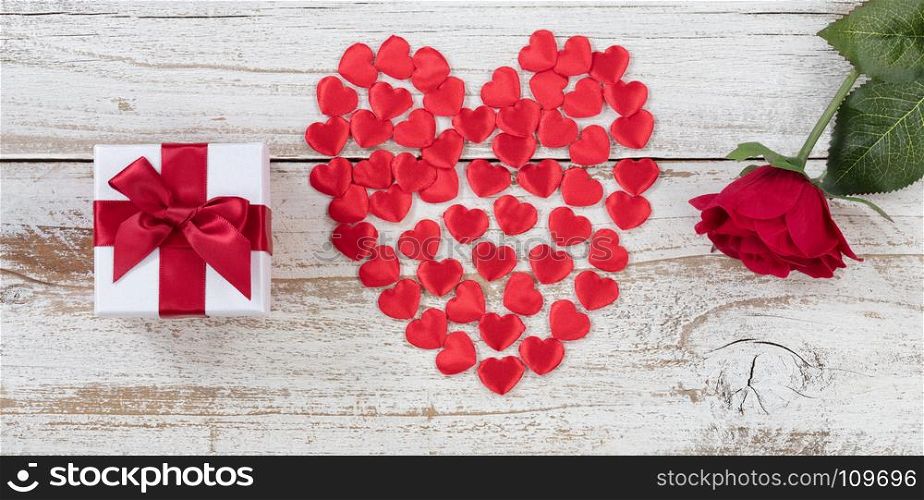 Filled red heart shapes, gift box and single rose on rustic white wood in flat lay view