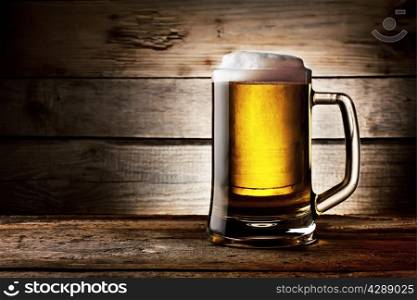 Filled with beer glass with white foam on background of wooden planks