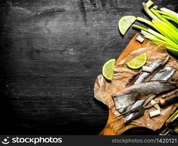 Fillet of pickled herring with lime and green onions. Black chalkboard.. Fillet of pickled herring