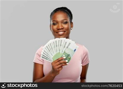 finance, currency and people concept - happy african american young woman holding hundreds of euro money banknotes over grey background. happy african american woman with euro money