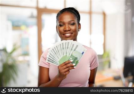finance, currency and people concept - happy african american young woman holding hundreds of euro money banknotes over office background. happy african american woman with euro money
