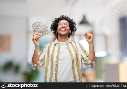 finance, currency and people concept - happy man holding hundreds of dollar money banknotes celebrating success over office background. happy man with money celebrating success at office
