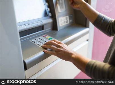 finance, money, bank and people concept - close up of hand entering pin code at atm machine
