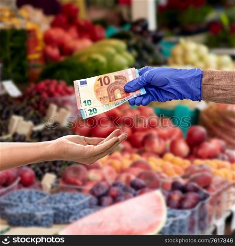 finance, payment and pandemic concept - close up of hand in medical glove giving money away over food at street market on background. close up of hand in medical glove giving money