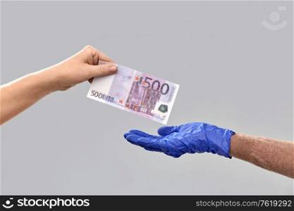 finance, payment and pandemic concept - close up of one hand giving money to another in medical glove over gray background. close up of hand in medical glove giving money