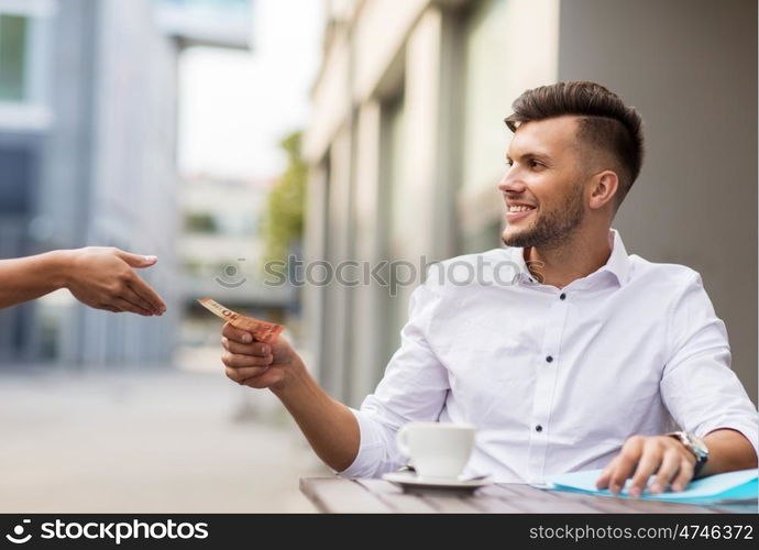 finance, payment, cash free and people concept - smiling young man with euro money paying for coffee at city street cafe