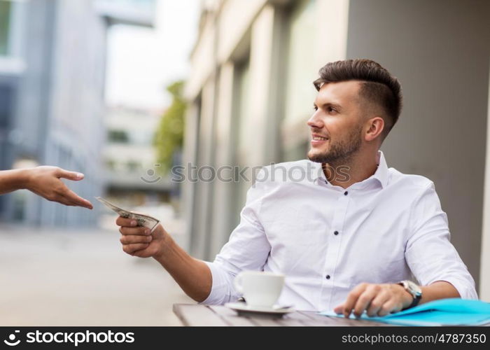 finance, payment, cash free and people concept - smiling young man with dollar money paying for coffee at city street cafe