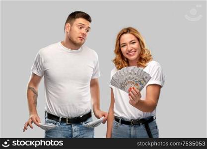 finance, saving and couple concept - happy young woman in white t-shirt holding dollar money and sad man with empty pockets over grey background. couple with money and empty pockets