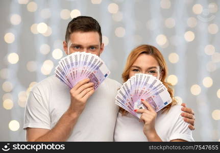 finance, saving and people concept - portrait of happy couple in white t-shirts with euro money over festive lights background. happy couple in white t-shirts with euro money