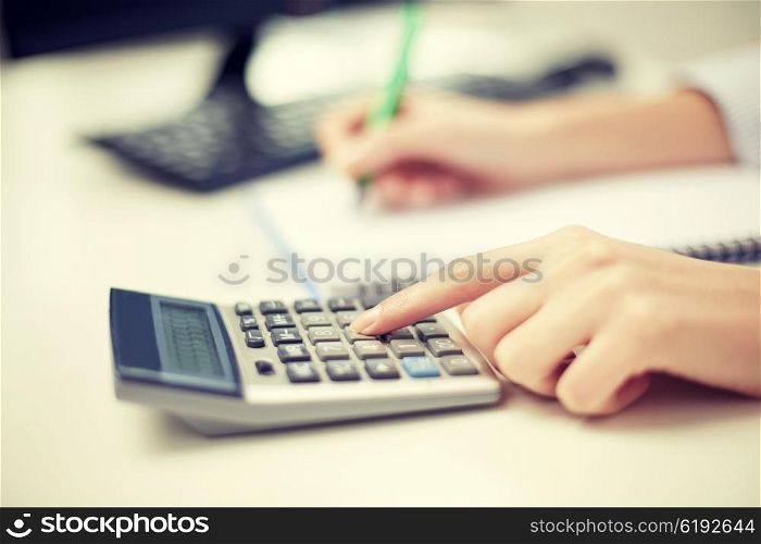 finances, economy, technology and people concept - close up of woman hands with calculator counting and taking notes to notebook