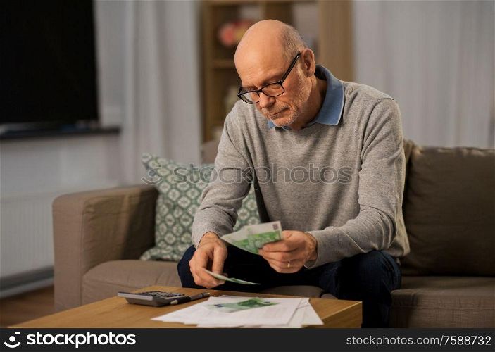 finances, savings and people concept - senior man with calculator and bills counting money at home in evening. senior man counting money at home