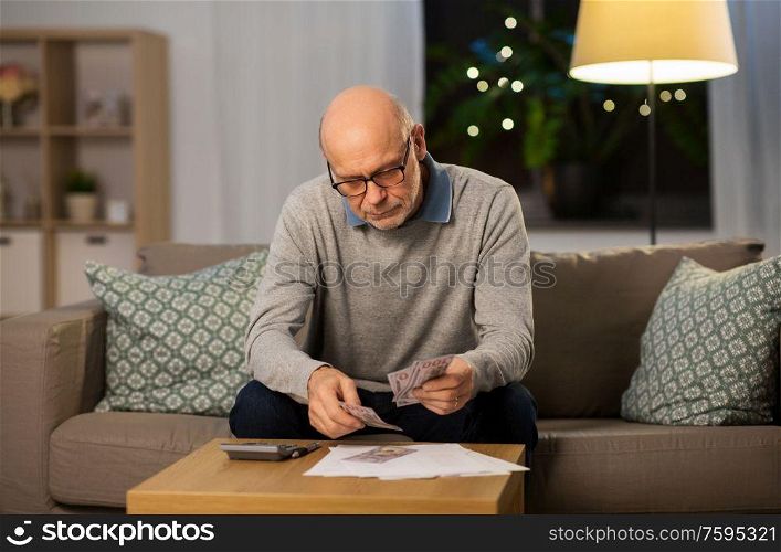 finances, savings and people concept - senior man with calculator and bills counting money at home in evening. senior man counting money at home