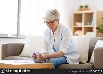 finances, savings, annuity insurance and people concept - senior woman with calculator and bills counting money at home. senior woman counting money at home