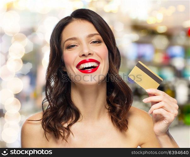 finances, shopping and people concept - happy smiling young woman with red lipstick holding credit card over lights background. beautiful woman with red lipstick and credit card