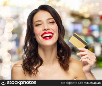 finances, shopping and people concept - happy smiling young woman with red lipstick holding credit card over lights background. beautiful woman with red lipstick and credit card