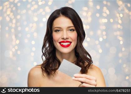 finances, shopping and people concept - happy smiling young woman with red lipstick holding credit card over holidays lights background. beautiful woman with red lipstick and credit card. beautiful woman with red lipstick and credit card