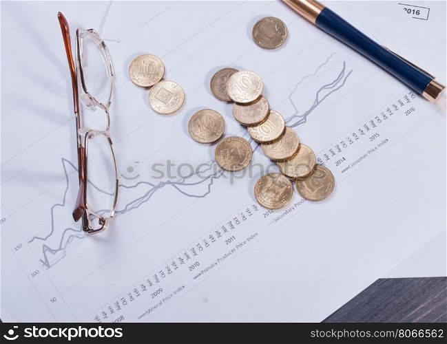 Financial charts lying on their spectacles, scattered coin and pen