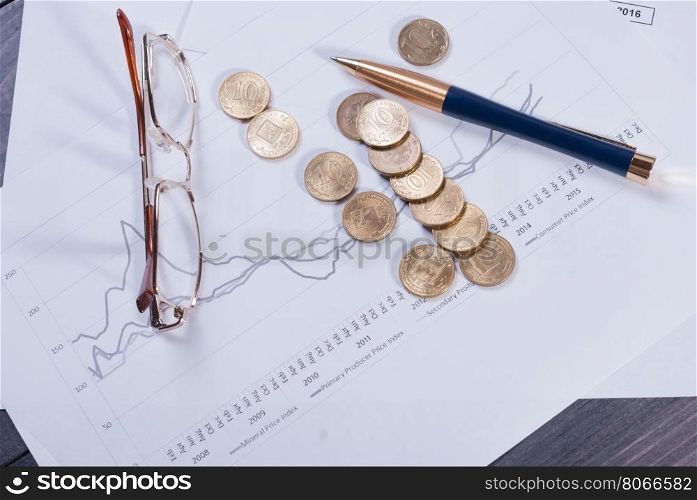 Financial charts lying on their spectacles, scattered coin and pen