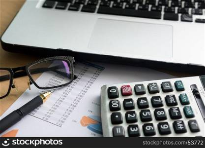 financial charts on the table with laptop, calculator, pen and glasses business concept.