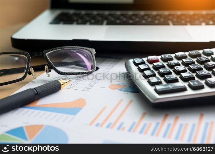 financial charts on the table with laptop, calculator, pen and glasses business concept.