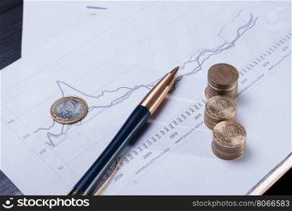 Financial charts with lying pen and stacks of coins.. Pen and coins lying on financial charts. The business concept.
