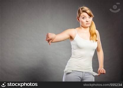 Financial difficulties, bad economy, no money concept. Young woman student girl showing empty pockets, thumb down sign gesture, sad unhappy face expression. Upset sad woman showing empty pockets