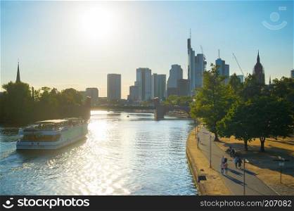 Financial district, cruise boat and people walking at embankment of the river Main at sunset. Frankfurt, Germany